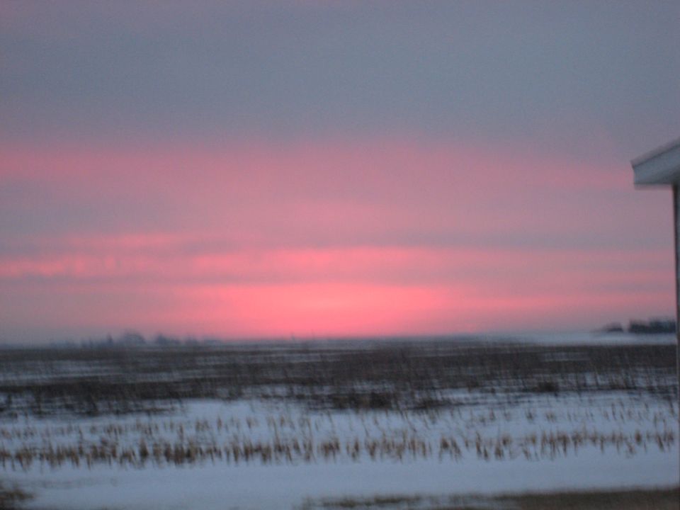 Pink and gray sky over a snowy field with a building corner