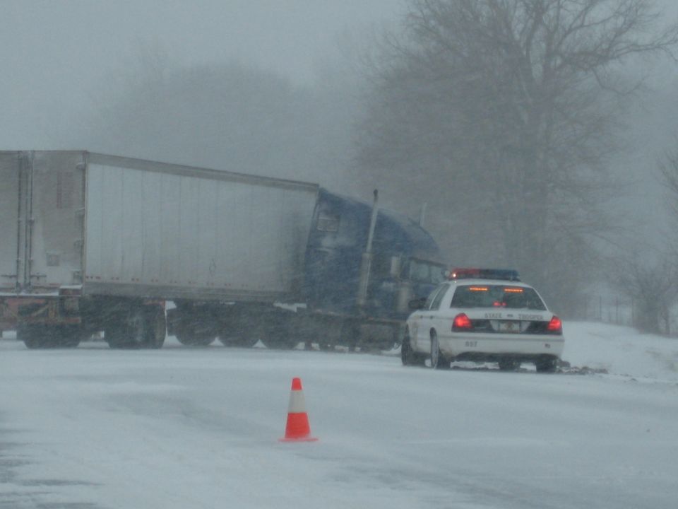 White 2001 Ford Crown Victoria police car in snow with a semi-truck behind it