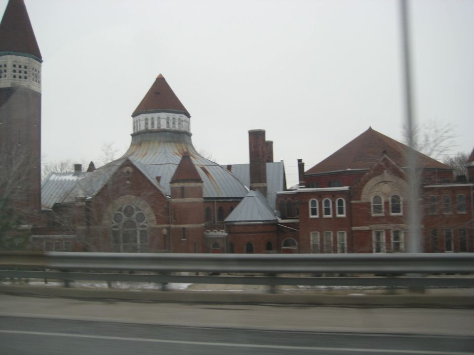 Brick building with a tall tower and domed roofs, seen from a highway overpass