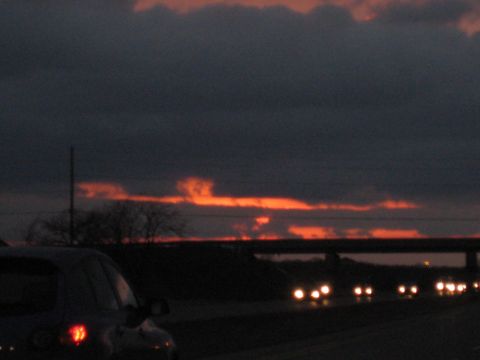 2001 Ford Crown Victoria - A dark sedan's rear taillight is visible as it drives on a highway at dusk.