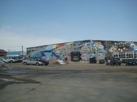 2001 Ford Crown Victoria - A building is covered in a vibrant mural, with several cars parked in the lot under a bright sky.