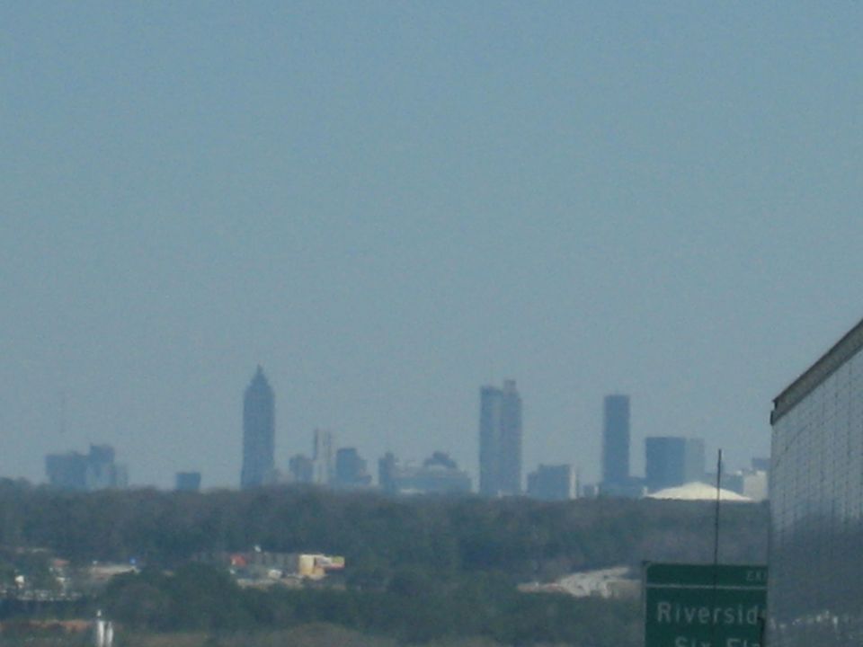 City skyline with tall buildings and trees in the foreground, a building on the right