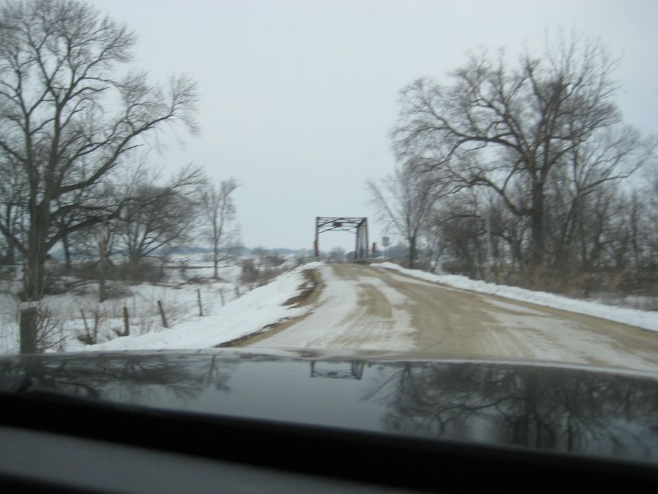 Dashboard reflection on a snowy road leading to a bridge