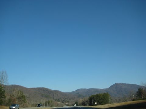 2001 Ford Crown Victoria - Two vehicles are visible on a highway passing through a mountainous, wooded area on a clear day.