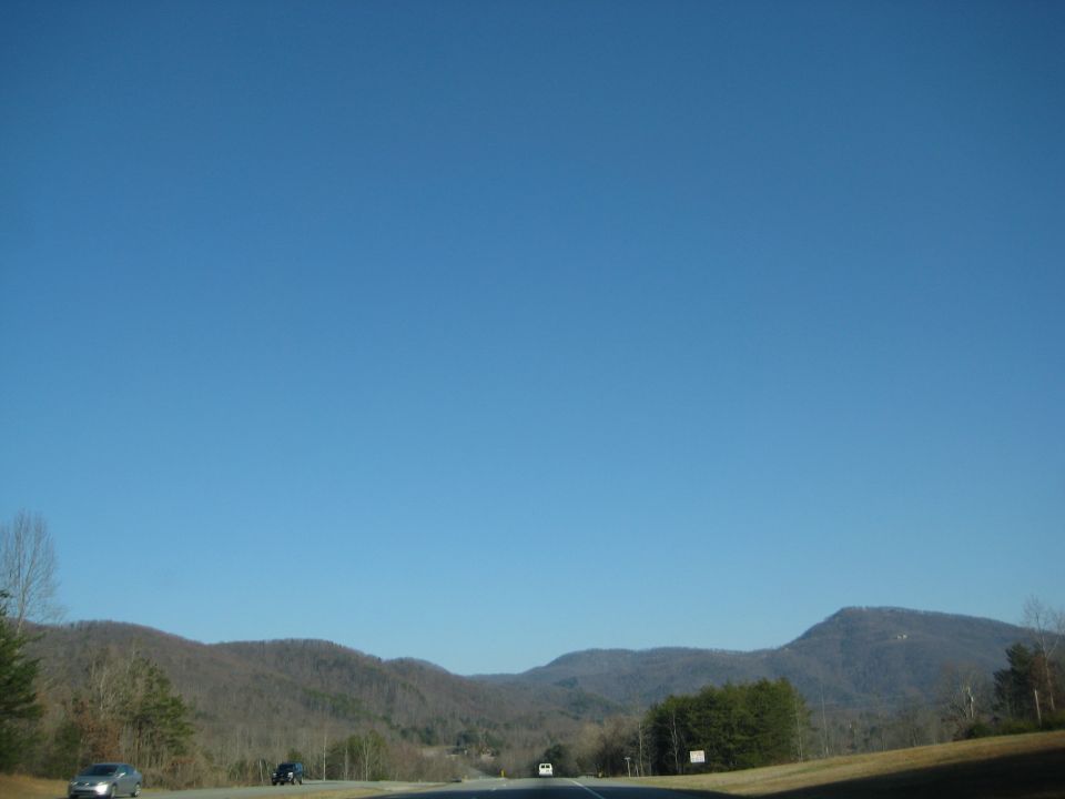 Cars driving on a highway with mountains in the background under a clear blue sky