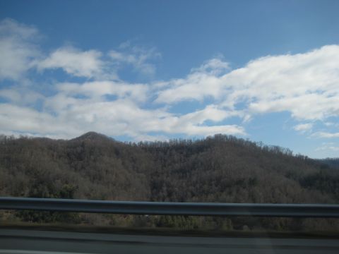 2001 Ford Crown Victoria - Mountain landscape with bare trees under a blue sky with scattered clouds. A metal guardrail is in the foreground.