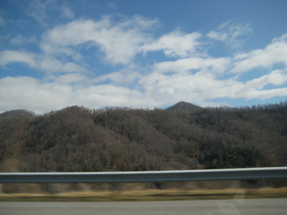 Mountainous landscape with a guardrail in the foreground and a blue sky with clouds