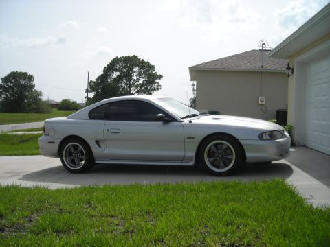 1998 Ford Mustang - A silver coupe is parked on a concrete driveway in front of a house.