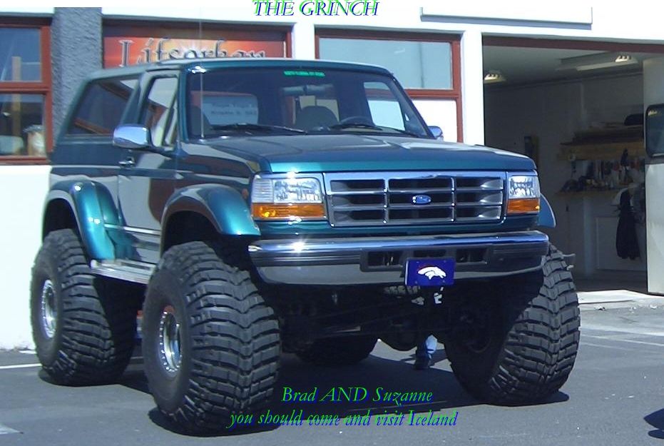 Lifted teal Ford Bronco SUV on huge tires parked outside a shop