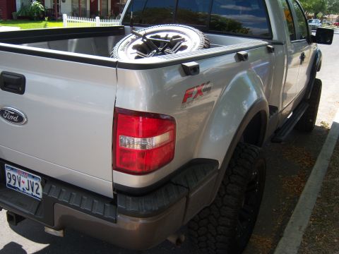 1979 Ford Bronco - Rear view of a silver Ford F-150 FX4 pickup truck with a spare tire in the bed.