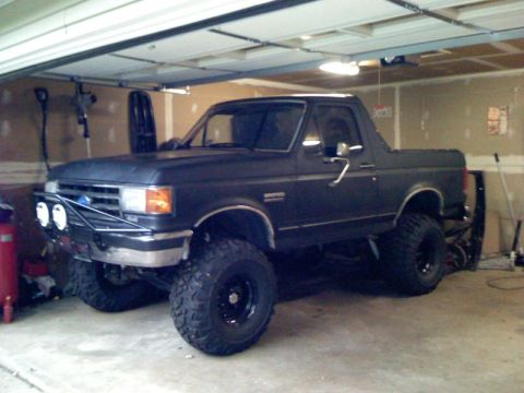 1989 Ford Bronco - This dark 1989 Ford Bronco is shown in a garage, an aftermarket bumper and lifted suspension with large tires.