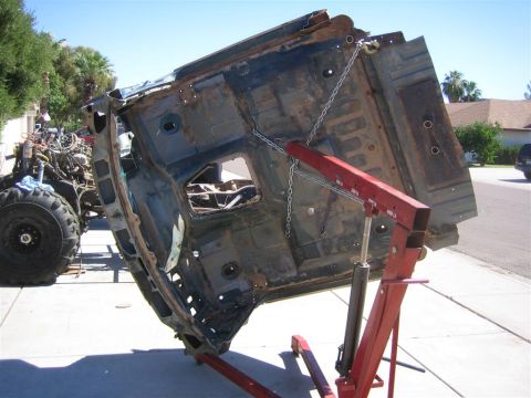 1994 Ford Bronco - Car body shell is being lifted by an engine hoist outdoors. Another vehicle's engine and tire are visible.