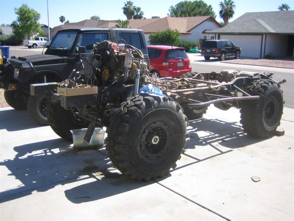 Stripped truck frame with mounted engine and solid axles on big mud tires in a driveway