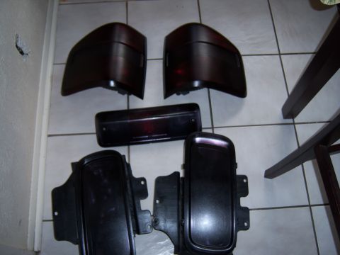 1979 Ford Bronco - Collection of automotive tail lights and trim parts on a tiled surface.