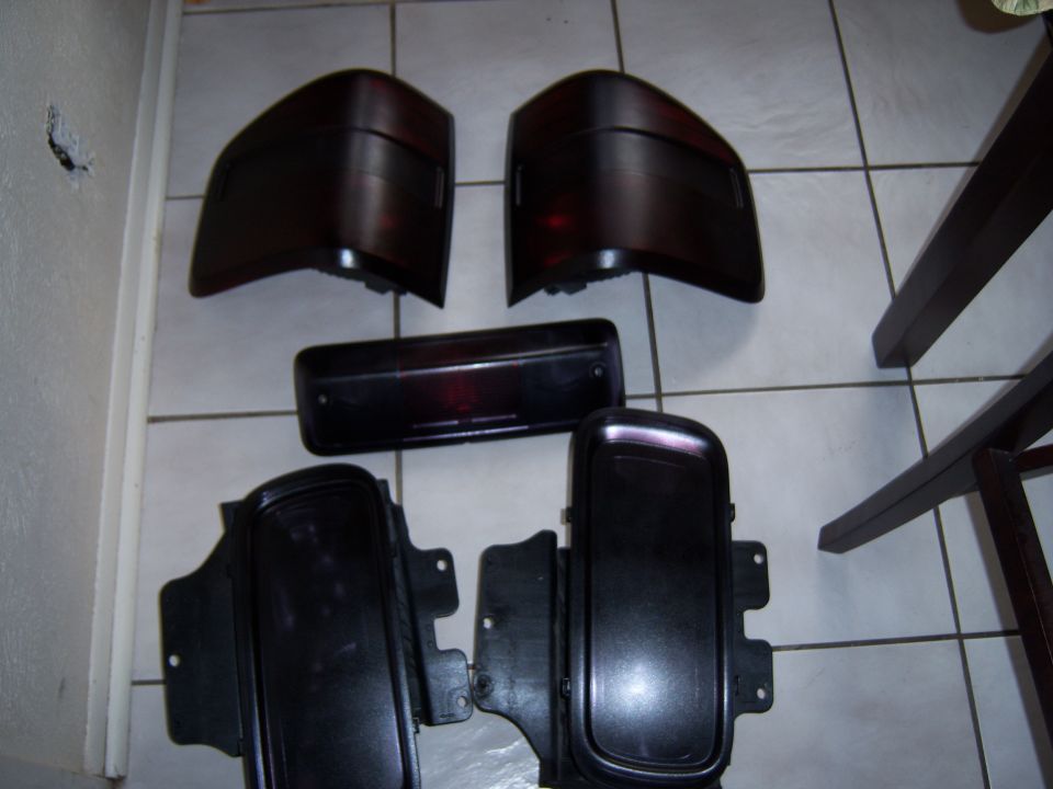 Several dark-colored car tail lights and black plastic trim pieces laid out on a tiled floor