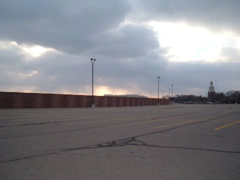 1971 Ford Ranchero - A wide view of an empty parking lot with a brick wall and a distant clock tower under a dramatic sky.