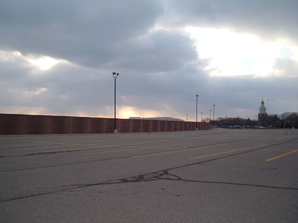 Empty parking lot with a brick wall on the left and a clock tower on the right under a cloudy sky