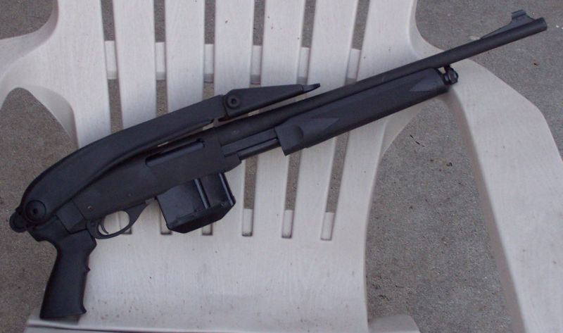 Black shotgun with pistol grip and detachable magazine resting on a white plastic chair
