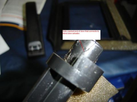 2007 Ford Mustang - Close-up of a removed black plastic HVAC blend door held up over a workbench, with an added red arrow and caption reading 'Note cracked end…