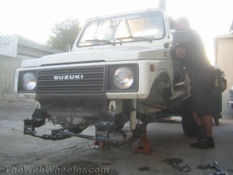 1987 Suzuki Samurai - A person works on the front axle of a Suzuki Samurai, which is raised on jack stands.