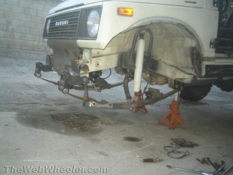 1987 Suzuki Samurai - Front suspension of a 1987 Suzuki Samurai is disassembled, showing leaf springs removed and the vehicle supported by jack stands.