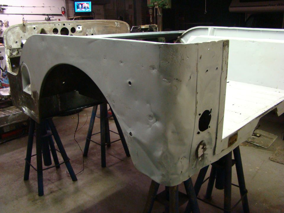White Jeep body panels, dented and unpainted, on blue sawhorses in a workshop