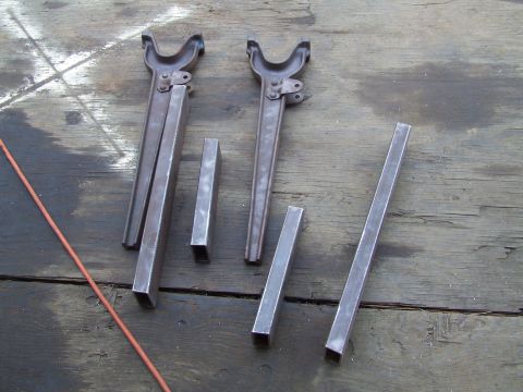 1967 Ford Bronco - Several metal components, possibly for a vehicle repair or fabrication project, are arranged on a weathered wooden surface.