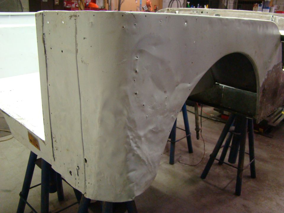 White Jeep CJ body tub section, showing rear fender area, supported by blue sawhorses in a workshop