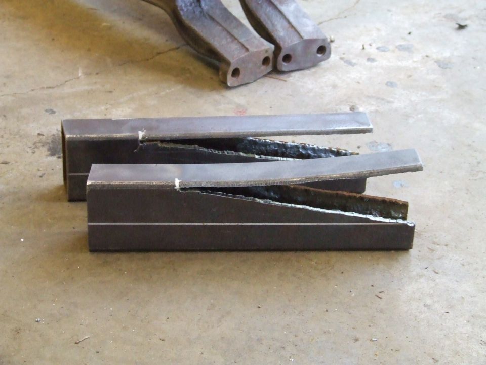 Two metal tubes cut lengthwise, showing rough welds inside. Another pair of metal parts is visible in the background