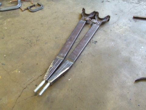 1967 Ford Bronco - Two fabricated metal suspension components rest on a concrete floor, possibly awaiting installation.