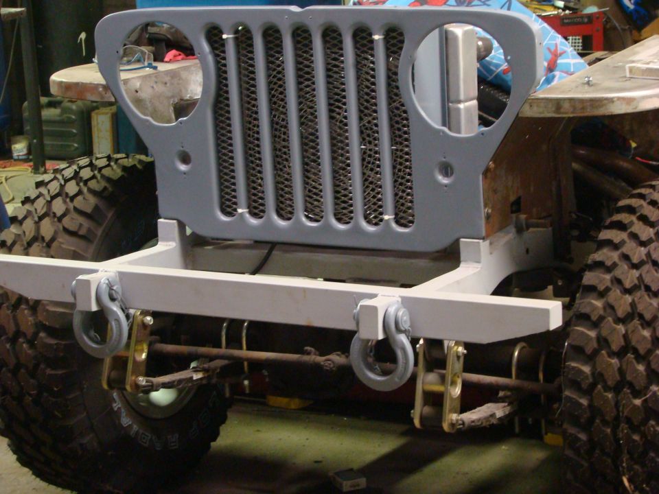 Gray primer Jeep CJ grille and front bumper with tow hooks, showing large off-road tires