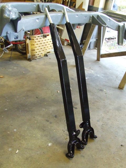 1967 Ford Bronco - A vehicle frame is supported by stands, with two newly painted black suspension parts positioned in front.