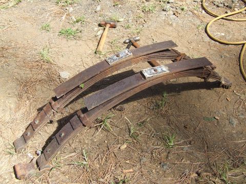 1967 Ford Bronco - Two old, rusty leaf springs lie on the ground next to two hammers.