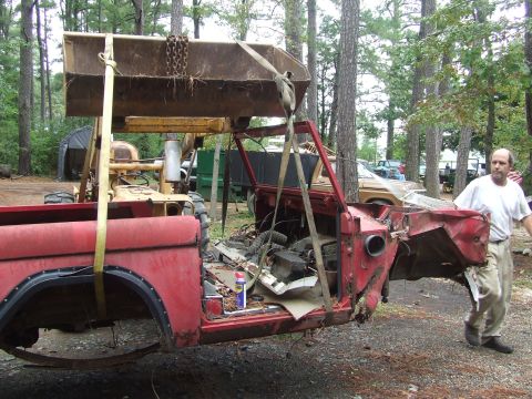 1967 Ford Bronco - A red 1967 Ford Bronco body is hoisted by a tractor, with a man standing nearby.