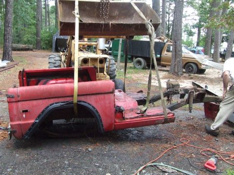 1967 Ford Bronco - A red vehicle body is being lifted by a loader, with another truck visible in the background.