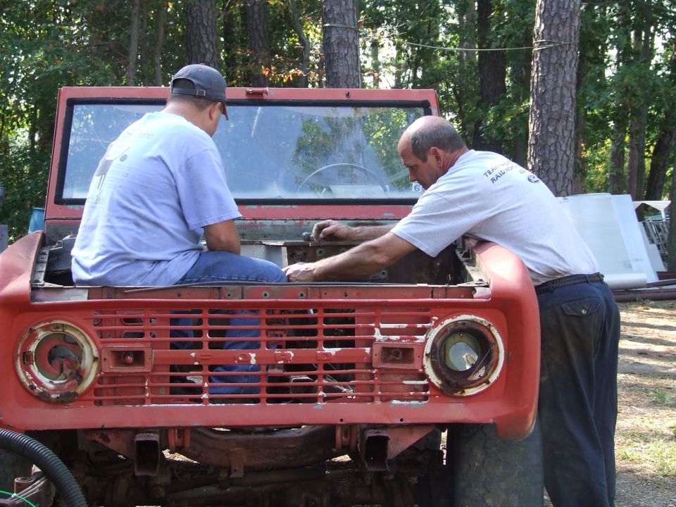 Red 1967 Ford Bronco front end with two men working on engine bay