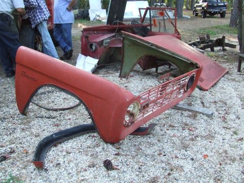 1967 Ford Bronco - Disassembled red Ford Bronco fender and grille are laid out on a gravel surface.