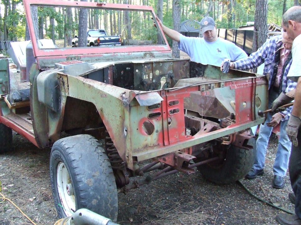 People working on a stripped-down Ford Bronco body, missing its hood and fenders
