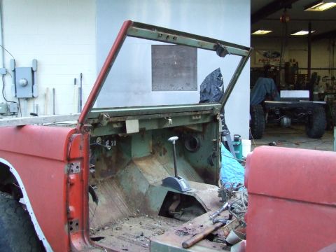 1967 Ford Bronco - The interior of a vintage Ford Bronco is exposed, showing significant rust and disrepair, with another vehicle in the background.