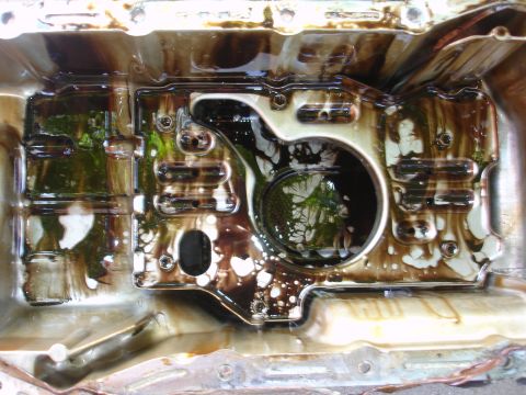 1993 Ford Taurus - Close-up of a heavily soiled automotive oil pan, showing accumulated sludge and debris.