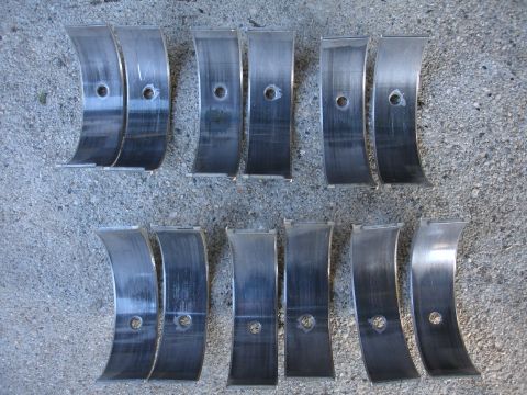 1993 Ford Taurus - Several engine bearing shells are laid out on a concrete surface, showing signs of wear.