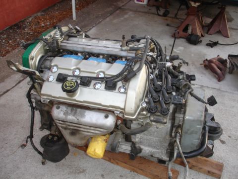 1993 Ford Taurus - A V6 engine assembly, likely removed from a vehicle, sits on wooden planks with various hoses and wiring attached parts attached.