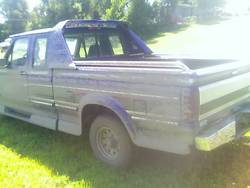 1995 Ford F-150 - A dark blue pickup truck with a camper shell is parked on a grassy area.
