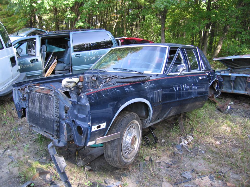 Wrecked dark blue sedan with grease-pencil markings in salvage yard