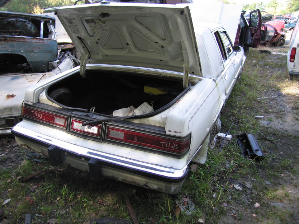 White Chrysler sedan with trunk open in salvage yard