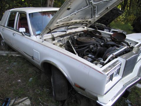 2001 Ford Crown Victoria - Photograph of a white Chrysler sedan engine bay in a junkyard, not a technical document.