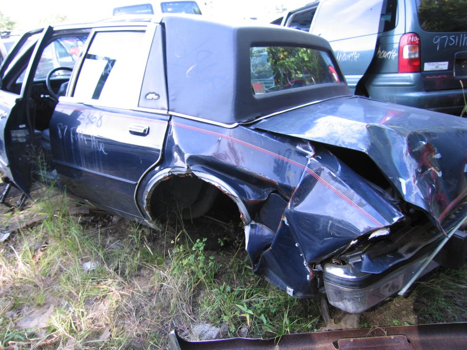 Wrecked dark blue sedan with crushed rear quarter in salvage yard