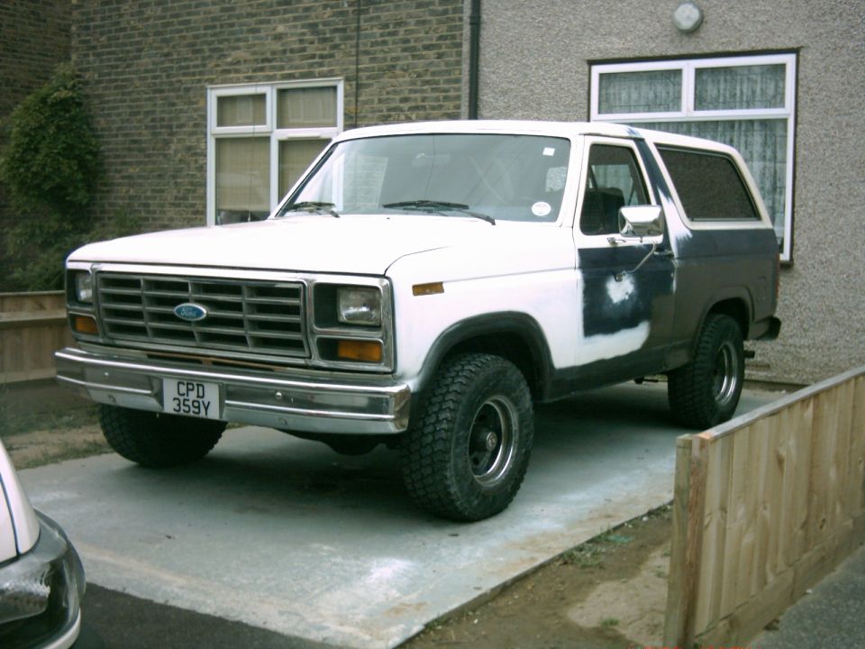 1982 Ford Bronco parked on a driveway, showing primer patches on the side.