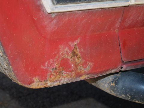 1996 Ford Bronco - A close-up view shows significant rust and damage on the lower rear quarter panel of a red vehicle, likely a Ford Bronco, with a black exha…