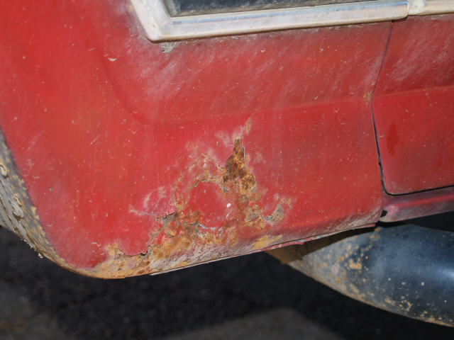 Close-up of rust on the lower rear quarter panel of a red vehicle.
